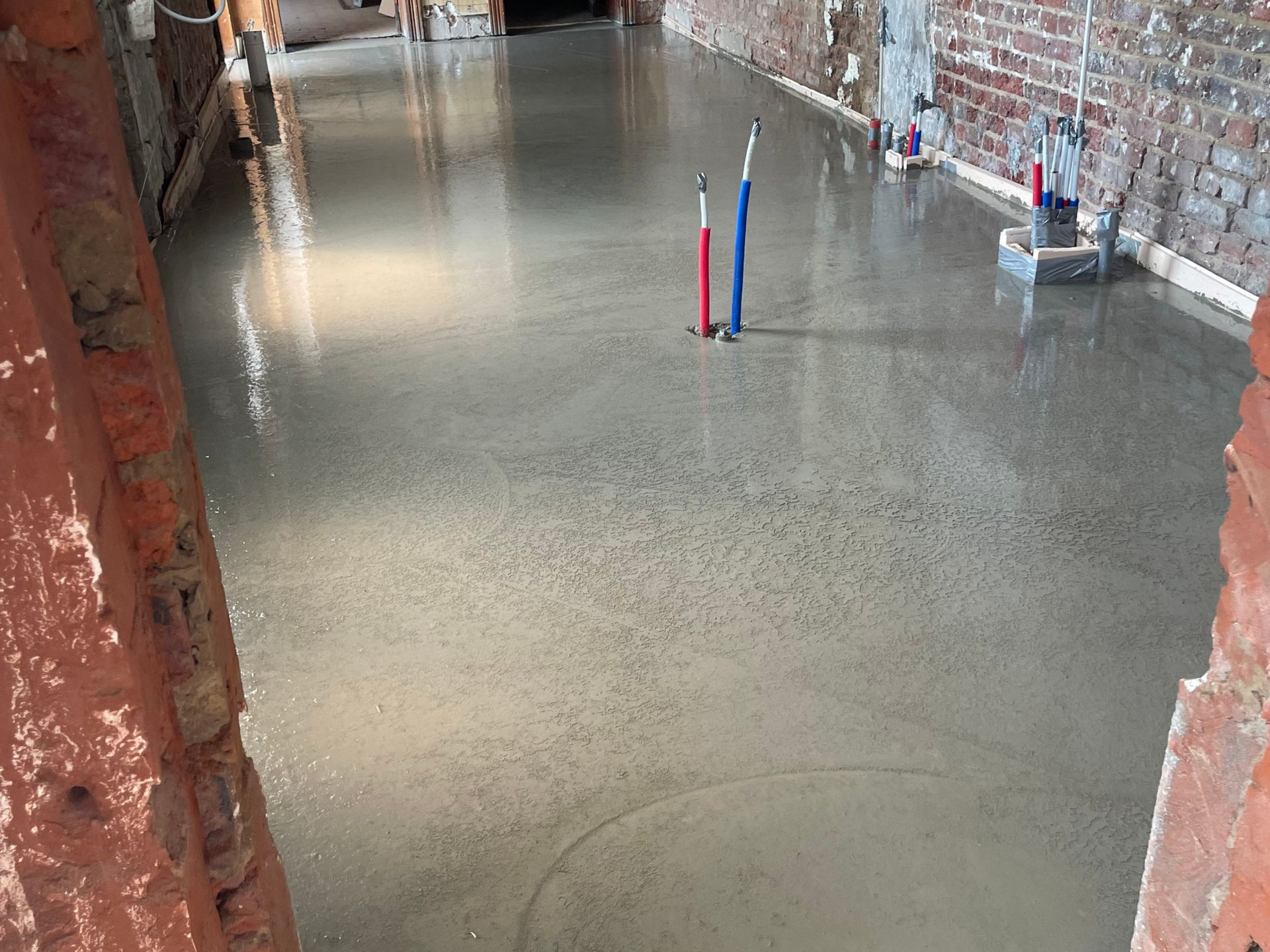 Sol en béton fraîchement coulé, murs en briques apparentes et canalisations.
