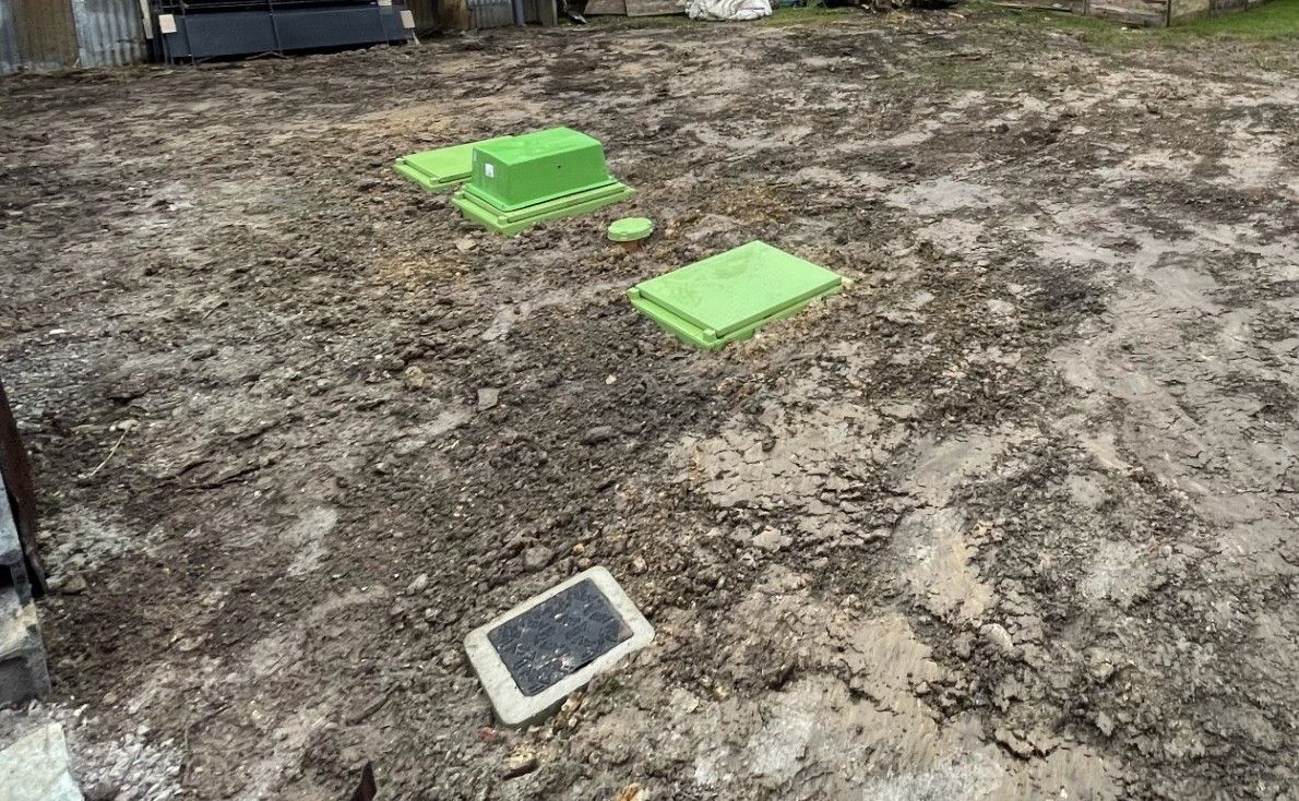 Une pelleteuse rouge creuse une tranchée, un tuyau bleu est visible dans le sol.