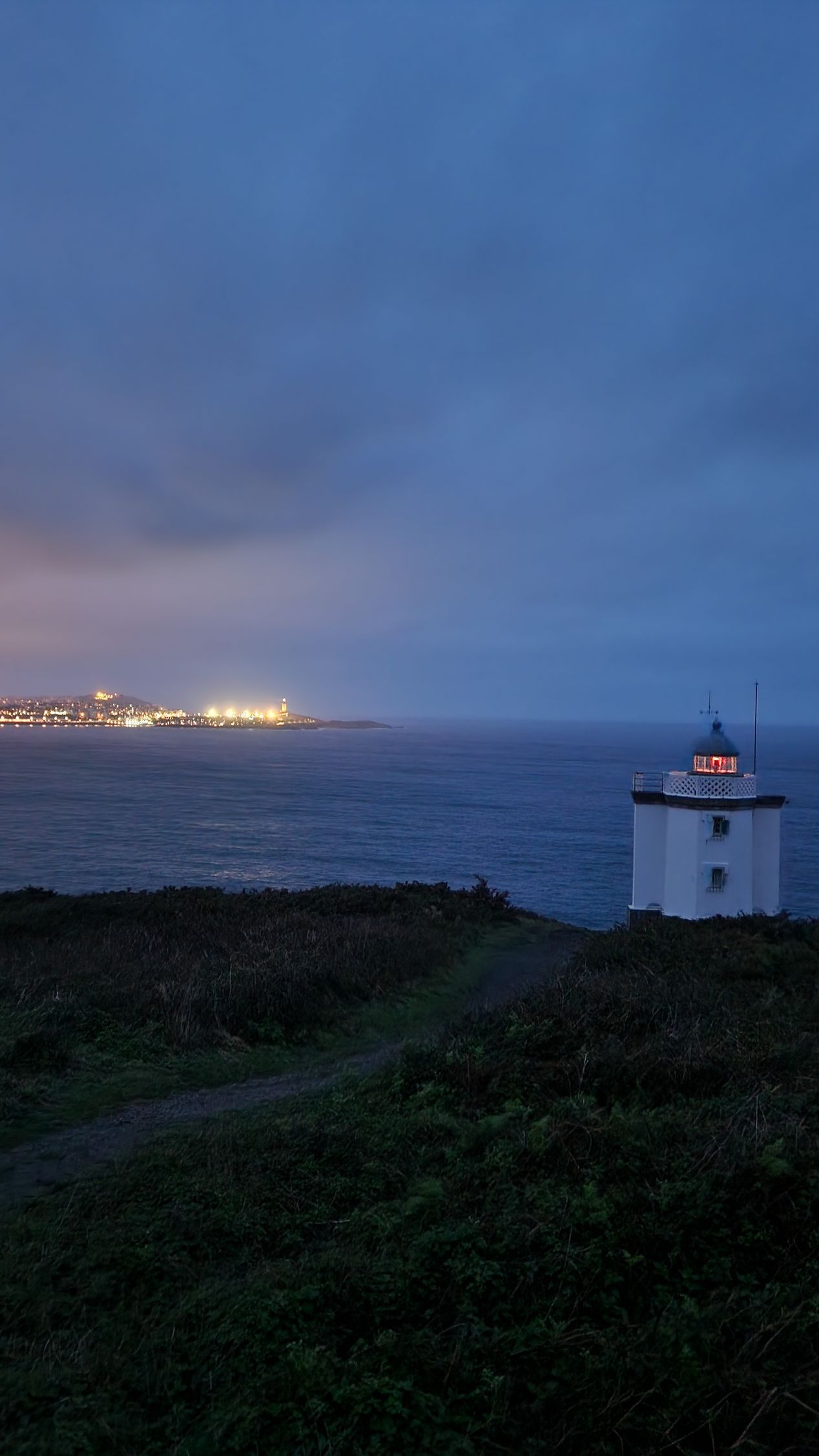 Un faro en una colina con vistas al océano por la noche.