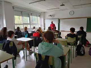 Un grupo de estudiantes están sentados en escritorios en un salón de clases.