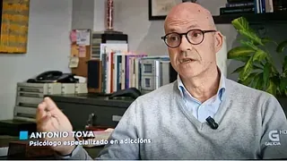 Un hombre calvo con gafas está sentado en un escritorio frente a una estantería.