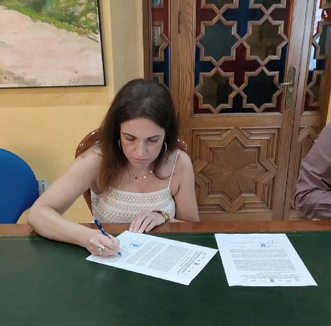 Una mujer está sentada en un escritorio escribiendo en un trozo de papel.