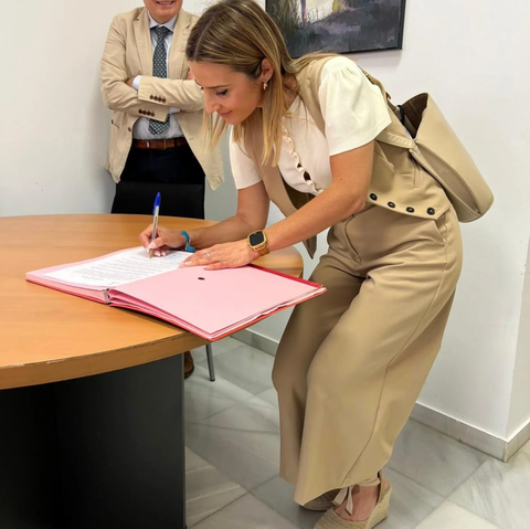 Una mujer está firmando un libro rosa sobre una mesa.
