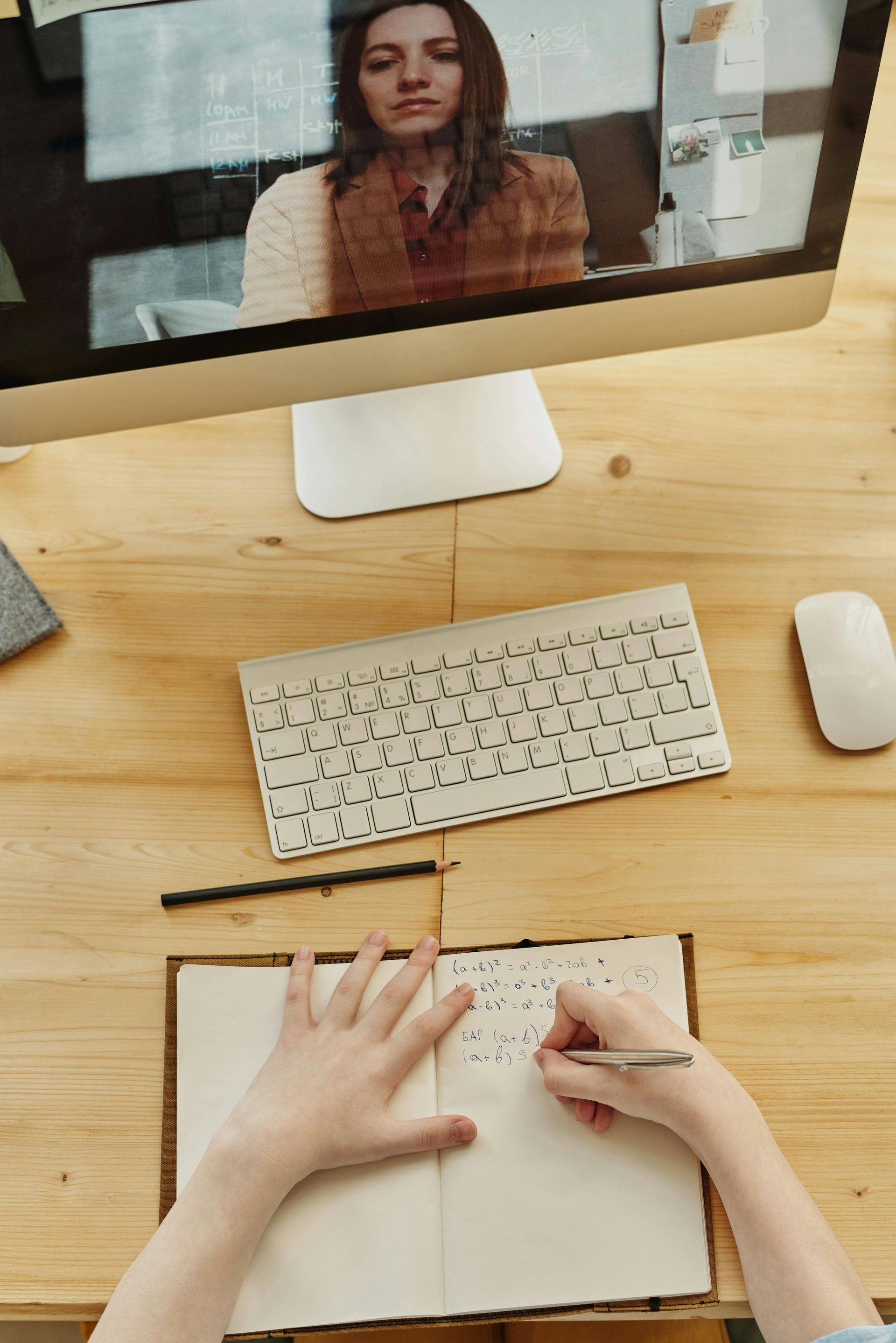 Una persona está sentada en un escritorio usando una computadora y escribiendo en un cuaderno.