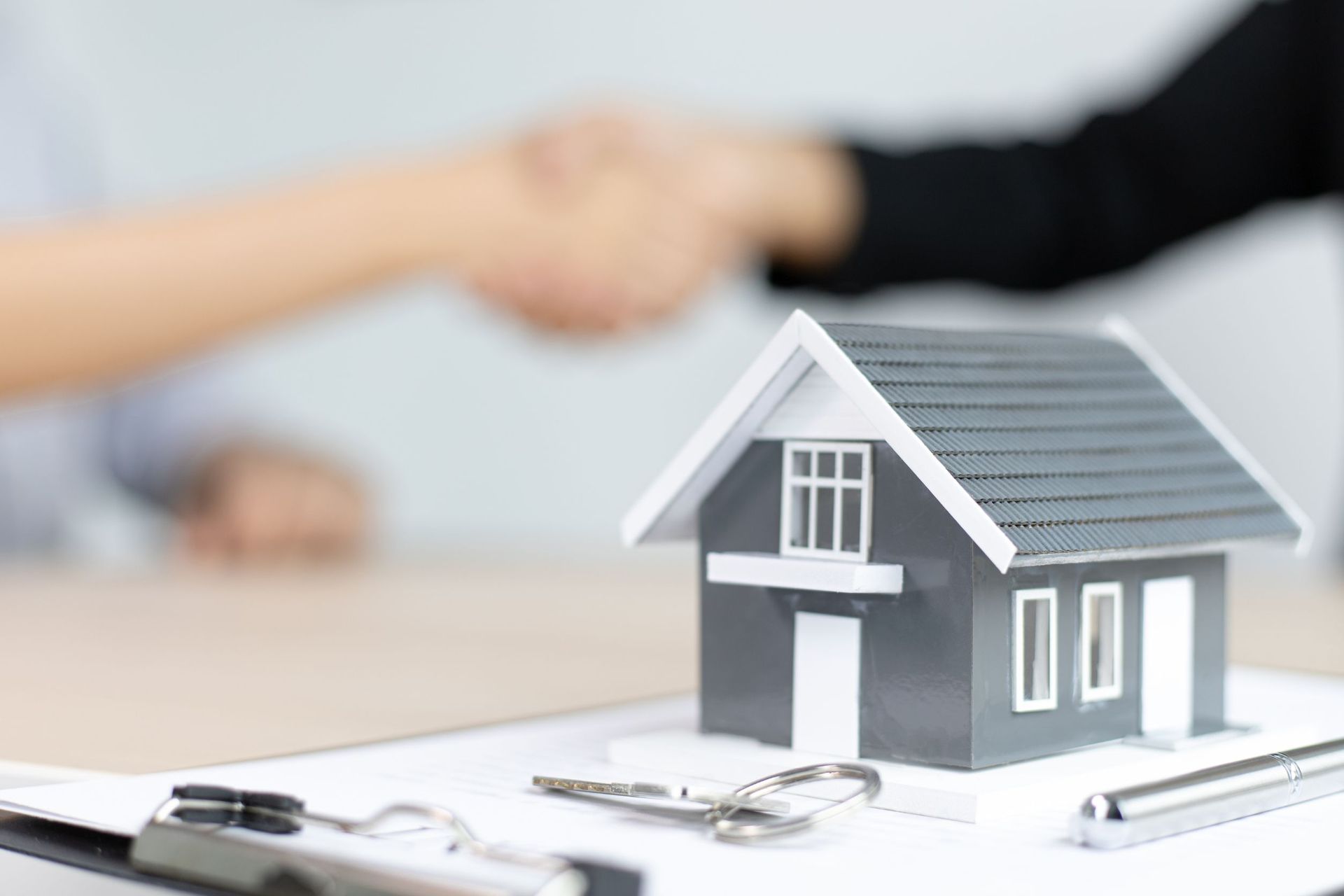 Una persona le da la mano a un agente inmobiliario frente a una casa modelo y unas llaves.