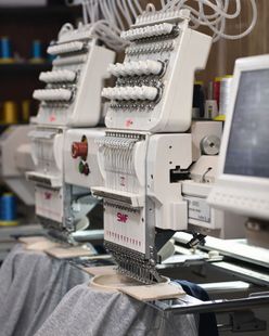Una persona con una sudadera blanca se ajusta una camiseta gris debajo de una máquina de prensado térmico.