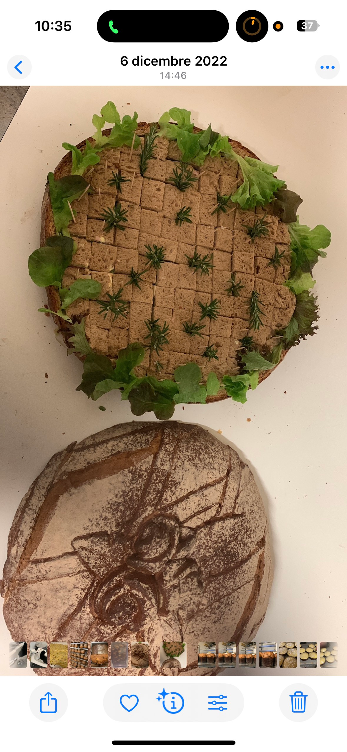 Un dolce rotondo con tre buchi ripieni di marmellata, spolverato con zucchero a velo, su carta dorata. Logo "Rovana".