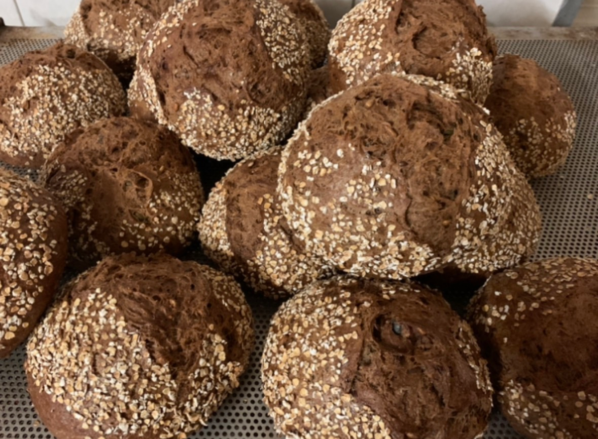 Primo piano di tre pagnotte di pane rustico con crosta dorata, in una scatola di cartone.
