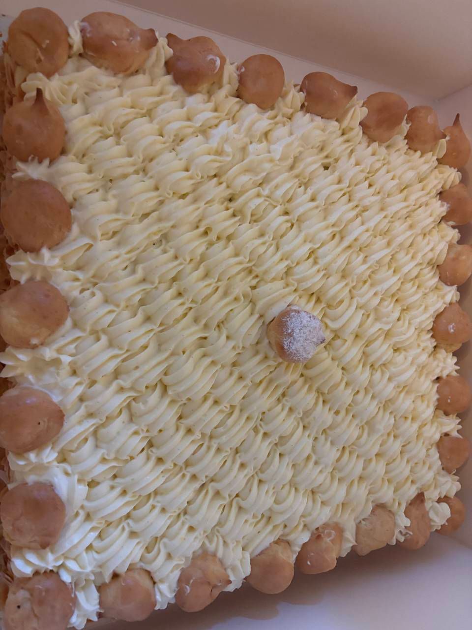 Torta quadrata, glassa alla crema con linee tratteggiate, decorata con bignè.
