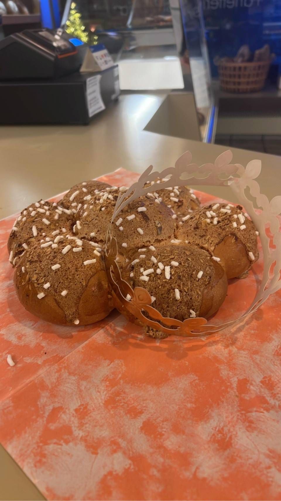 Pane integrale con granella bianca su un centrino di carta arancione, sullo sfondo l'interno di un negozio.