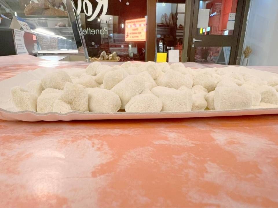 Vassoio di gnocchi quadrati infarinati su un tavolo color salmone, davanti alla finestra di un ristorante.