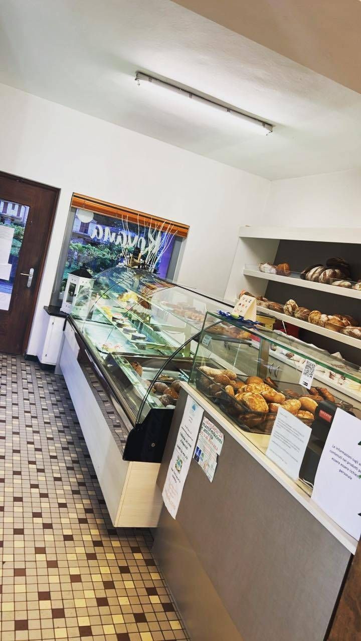 Interno di un panificio: vetrina con dolci, prodotti da forno sugli scaffali, pavimento piastrellato, porta e finestra.