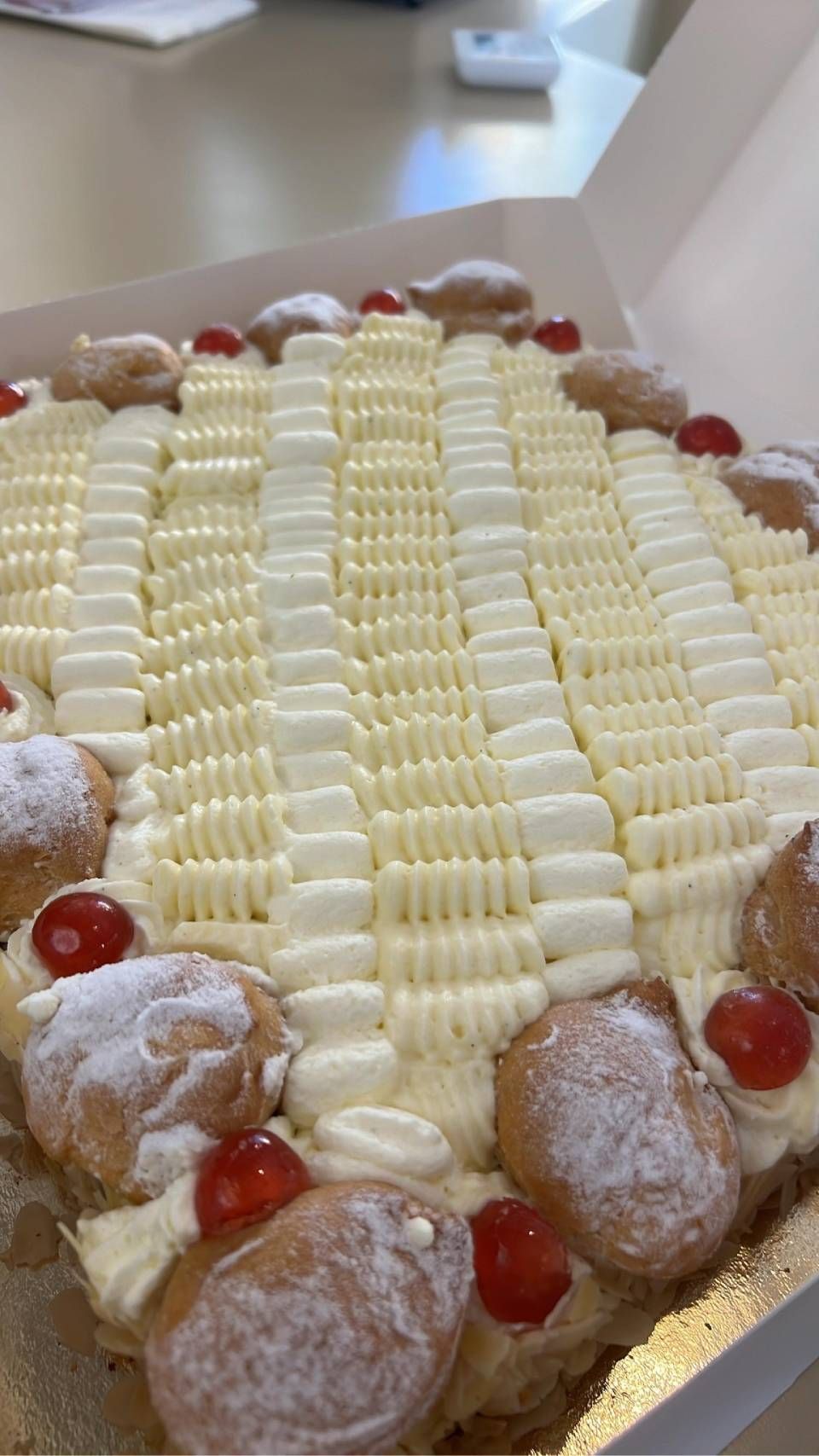Torta quadrata alla crema con glassa decorata, pasta sfoglia e ciliegie, in una scatola aperta.