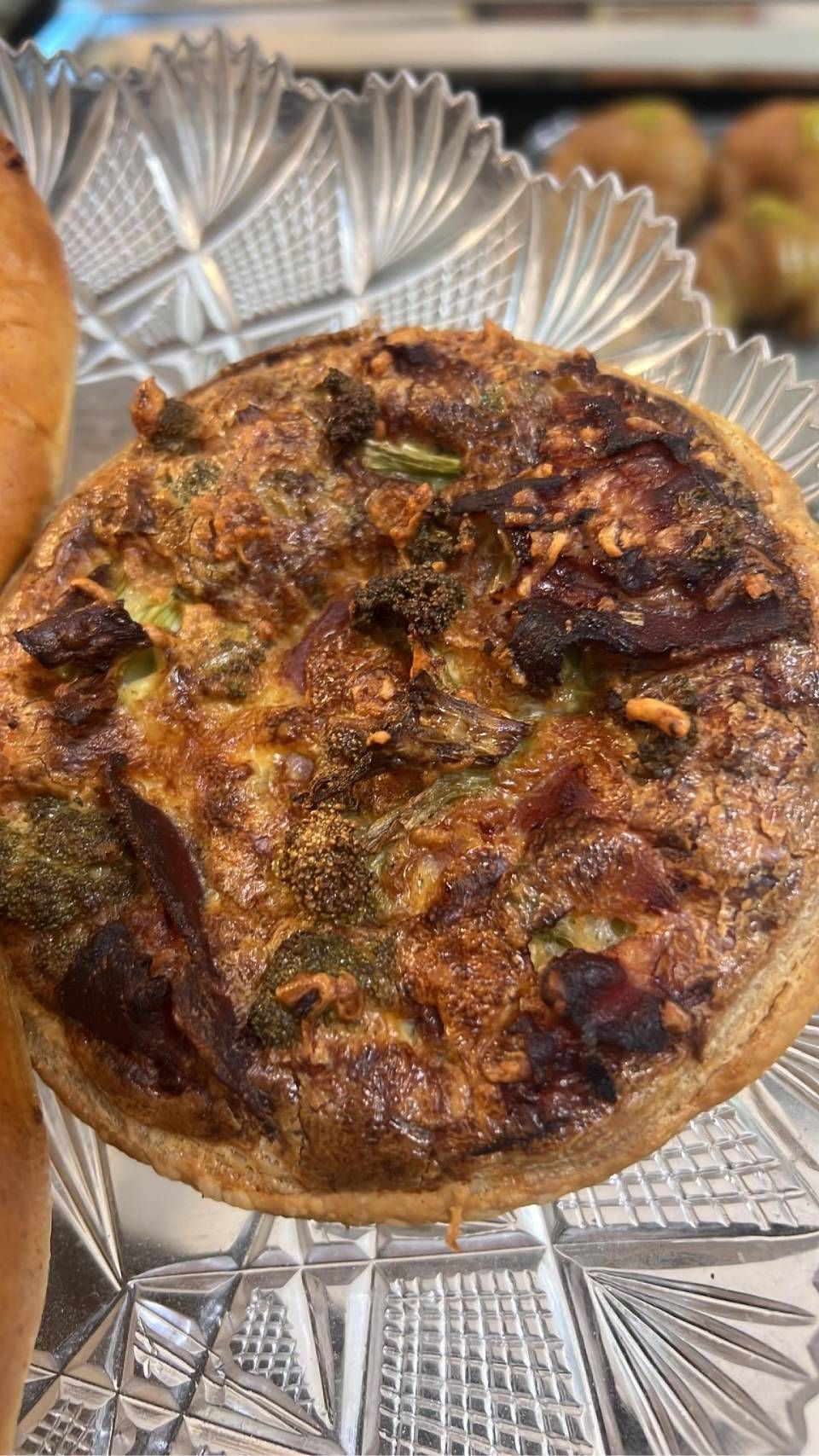 Torta salata su un piatto di vetro decorativo, con ripieno visibile e superficie dorata.