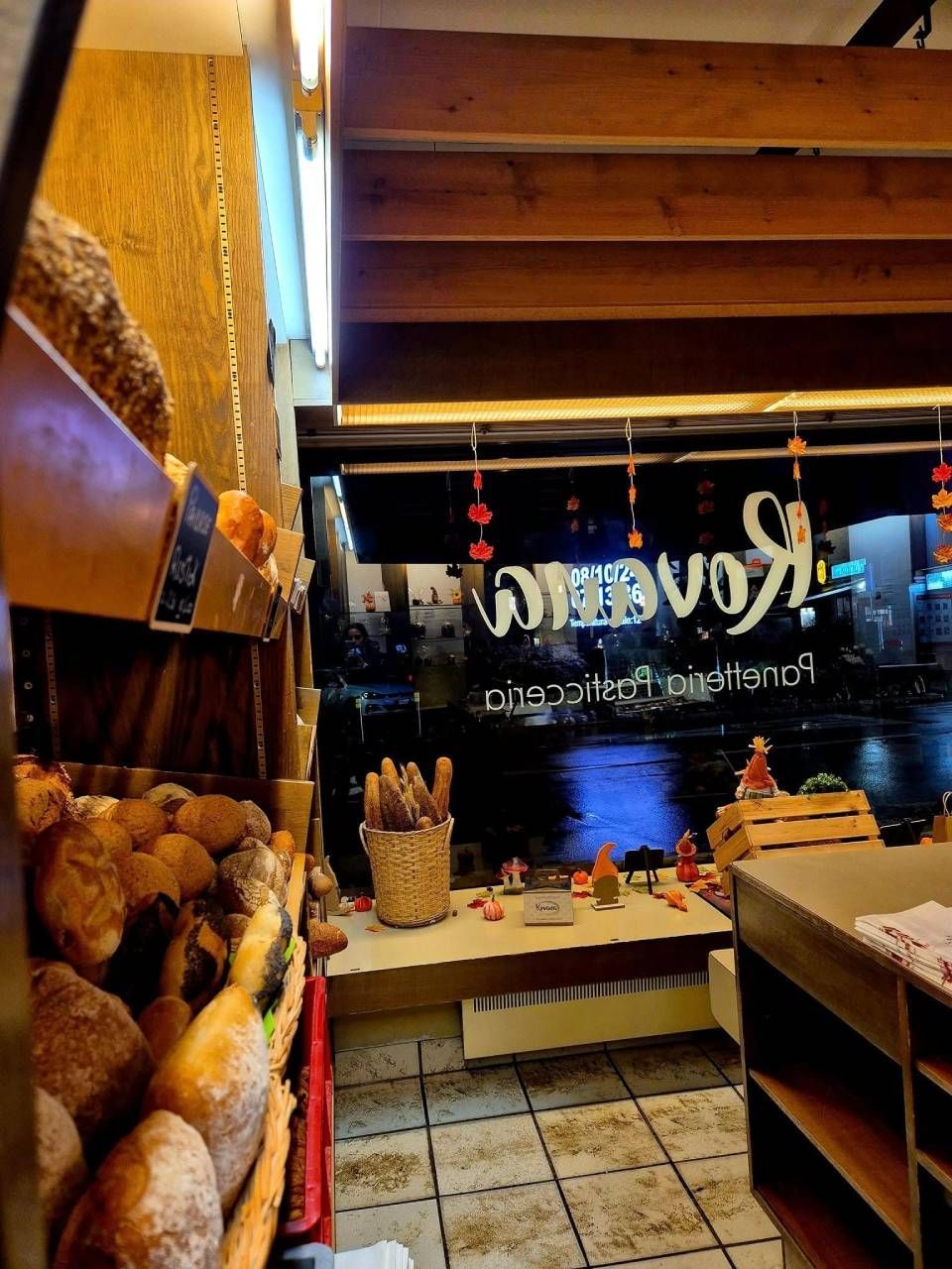 Interno di un panificio con pagnotte, cestino di vimini e finestra che mostra una strada cittadina di notte.