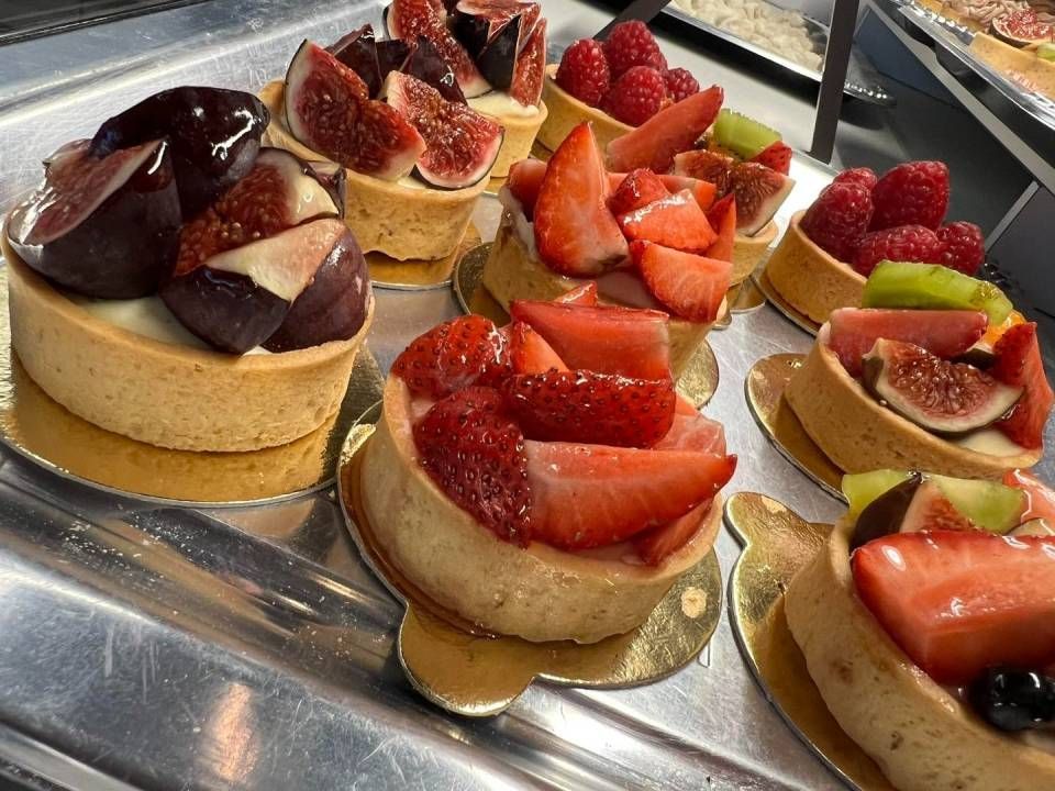 Crostate di frutta in esposizione, con fichi, fragole e lamponi. Le crostate dorate sono disposte su un vassoio di metallo.