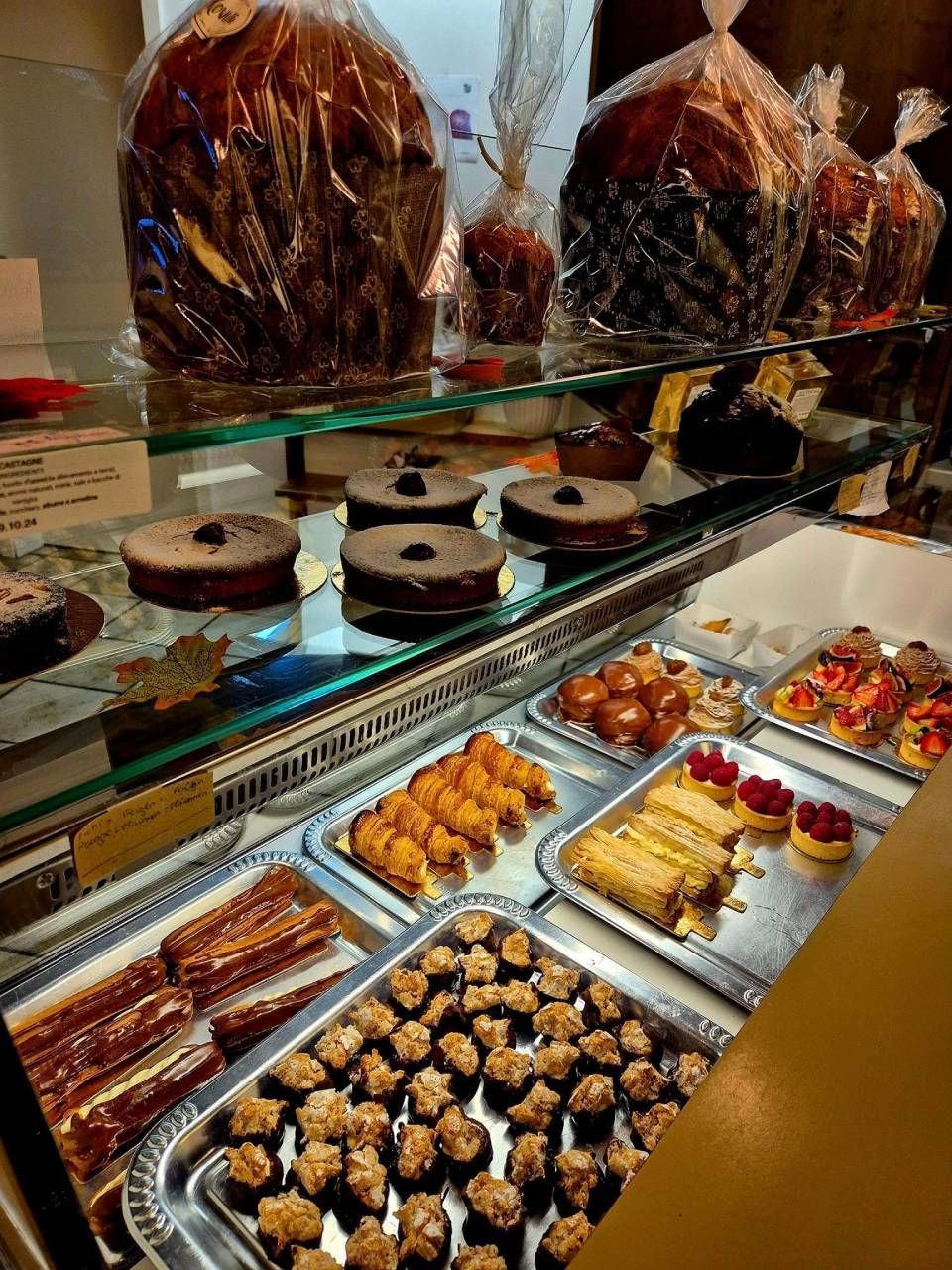 Esposizione di dolci: torte, biscotti e altri dessert in una vetrina di vetro, compresi articoli avvolti in cellophane.