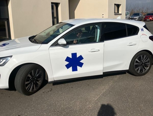 Voiture blanche avec logo médical en forme d'étoile bleue.