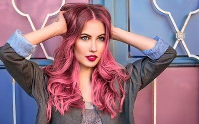 Una mujer con cabello rosa está parada frente a una pared colorida.