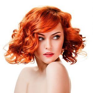 Una mujer con cabello rojo y rizado está mirando a la cámara.