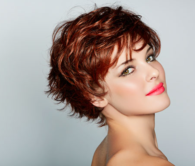 Una mujer con cabello corto rojo y lápiz labial rosa está sonriendo.