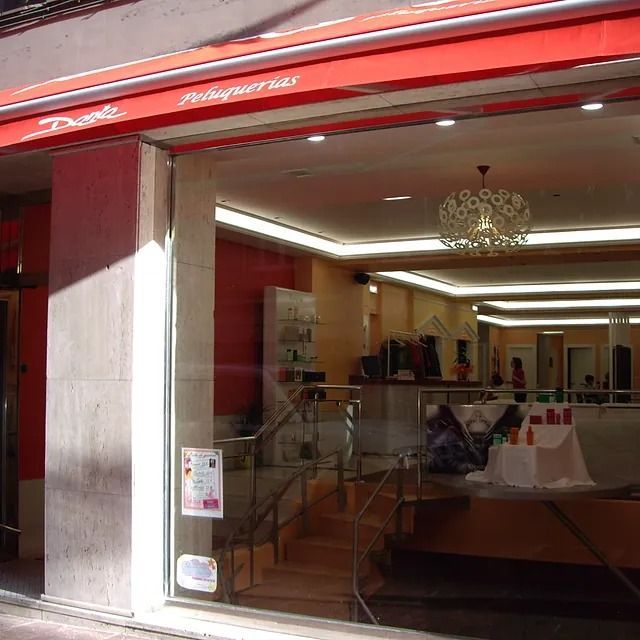 Una tienda con un toldo rojo que dice 'peluquería'.