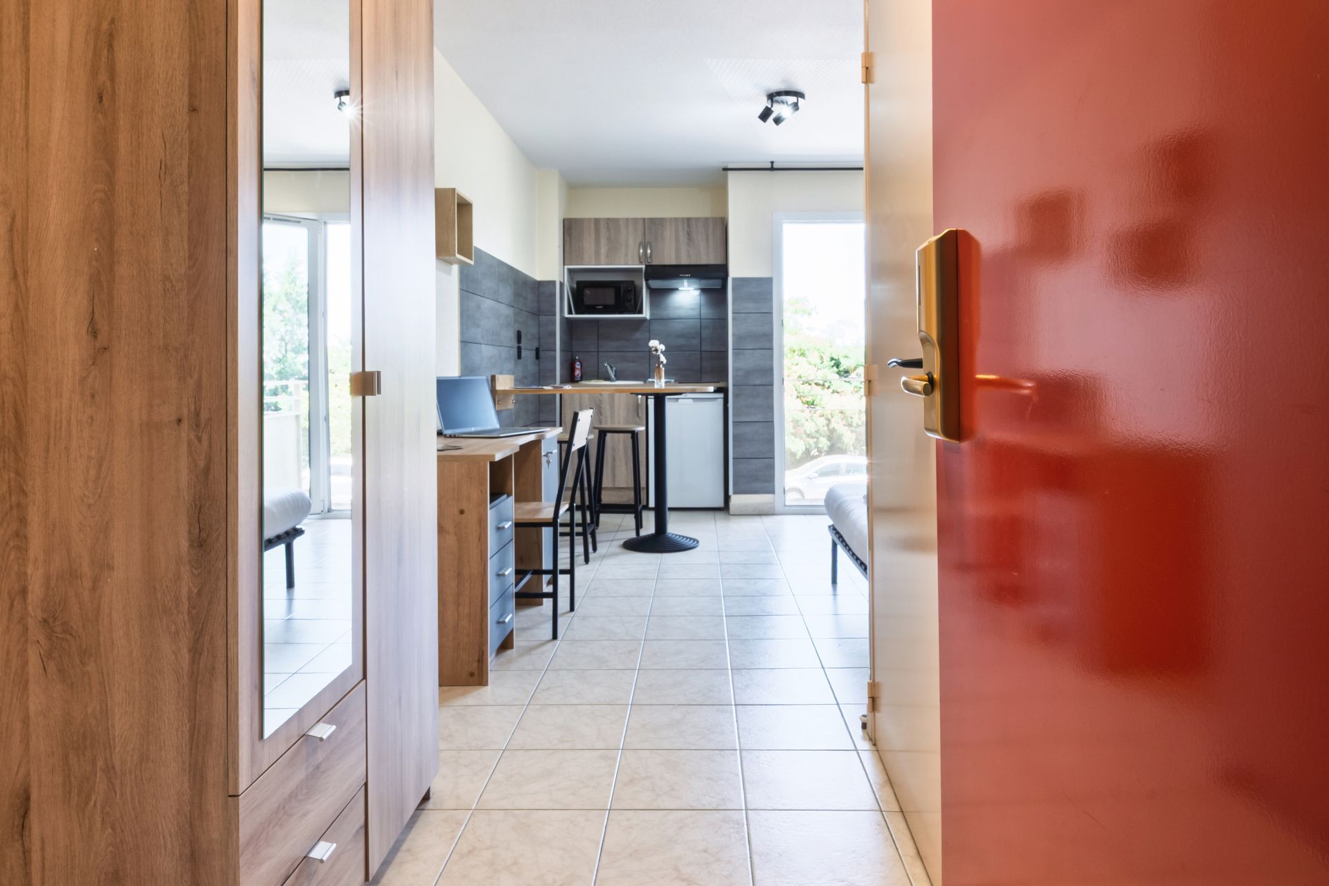 Vue à travers une porte donnant sur une cuisine moderne avec un sol carrelé blanc et des placards foncés.