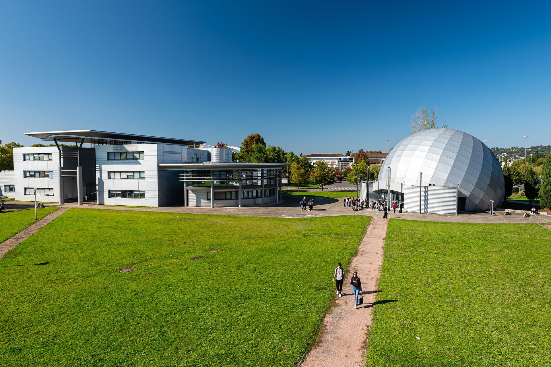 Campus moderne avec pelouse, allée et bâtiment à dôme argenté sous un ciel bleu azur