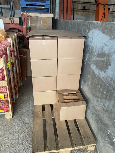Des cartons empilés sur une palette dans une allée d'entrepôt, à côté d'étagères et d'un mur en béton.