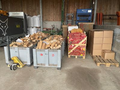 Entrepôt avec des bacs de chutes de bois, une caisse de fruits et légumes rouges et des cartons empilés sur des palettes.