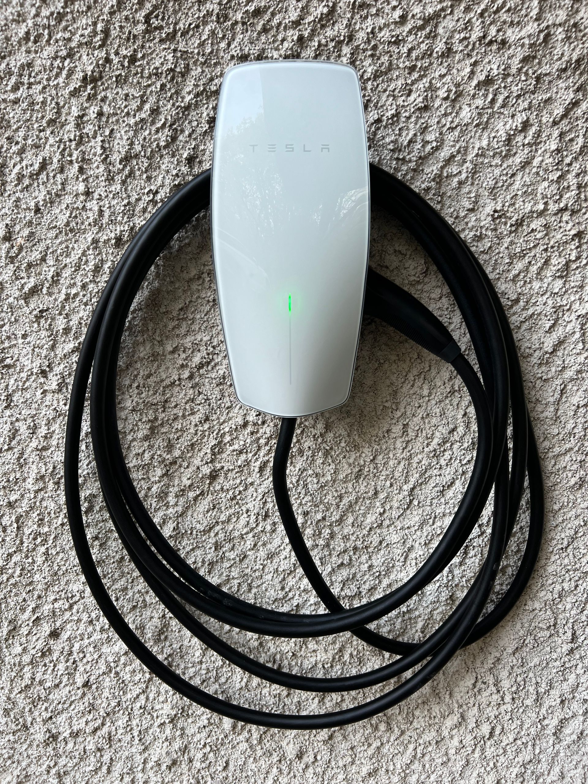 Borne de recharge électrique avec une lumière verte et un câble noir enroulé.