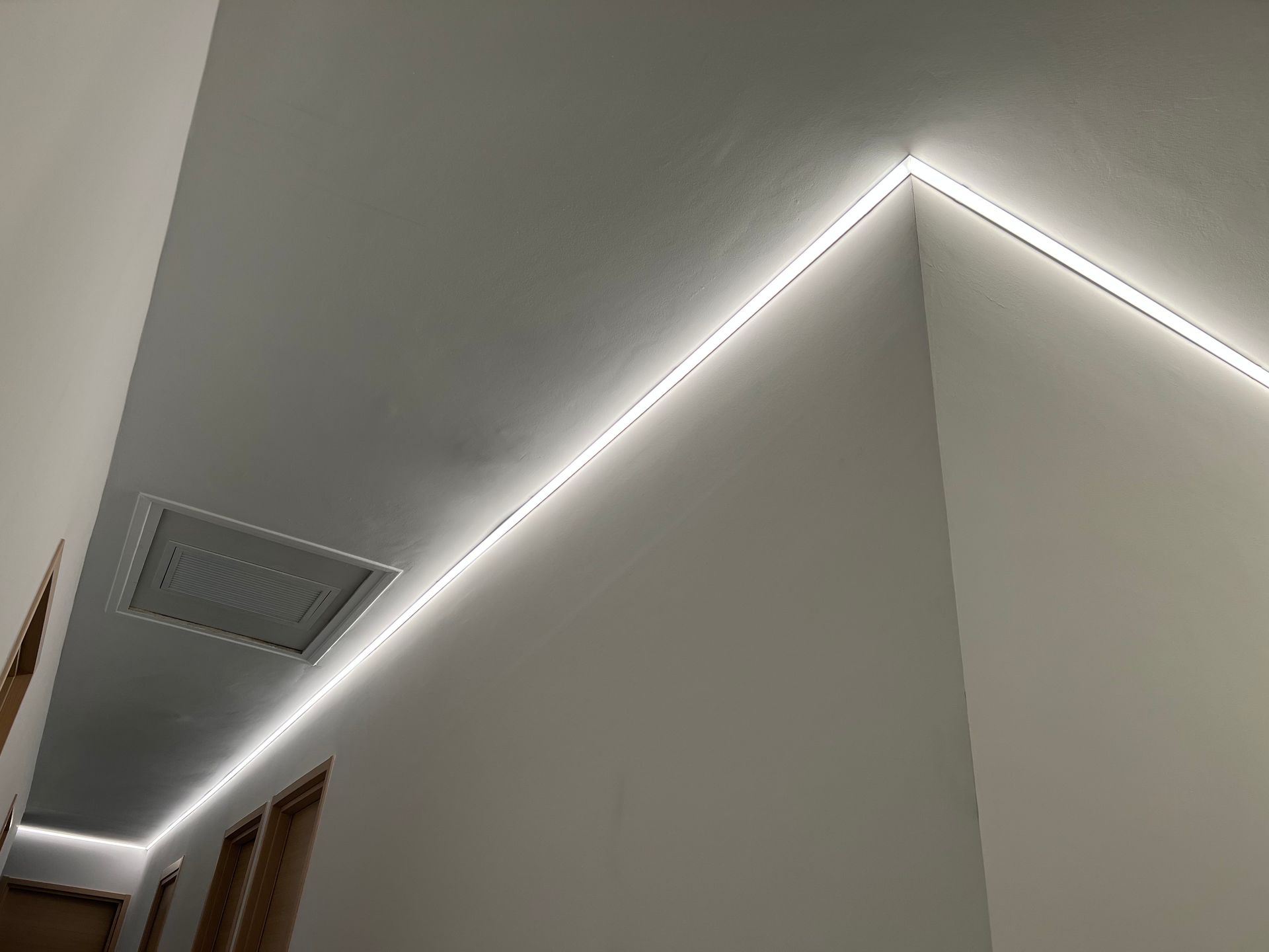 Coin de plafond avec éclairage LED, murs gris et grille d'aération dans un intérieur minimaliste