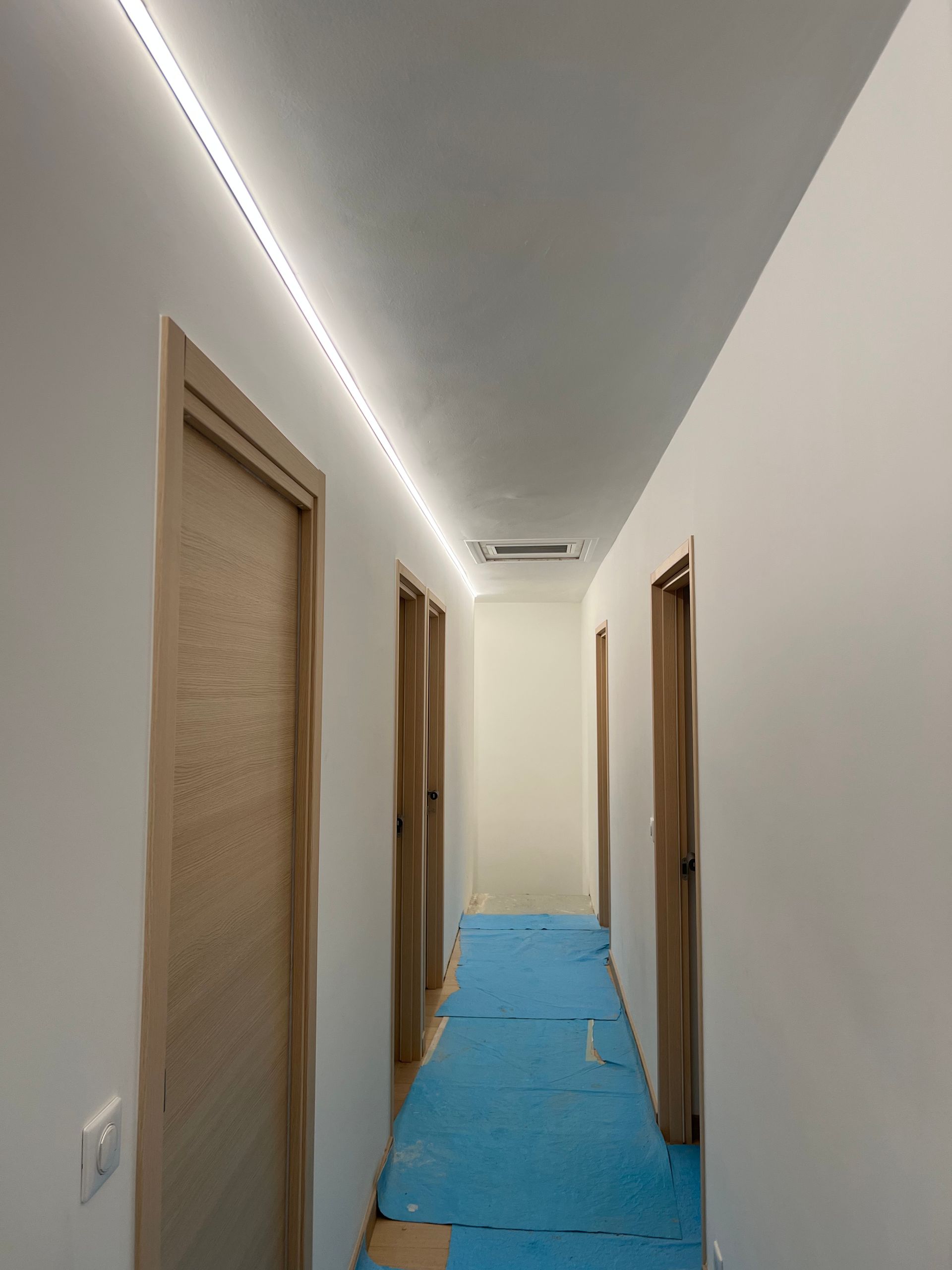 Couloir étroit avec portes beiges, murs blancs et revêtement de sol bleu en construction