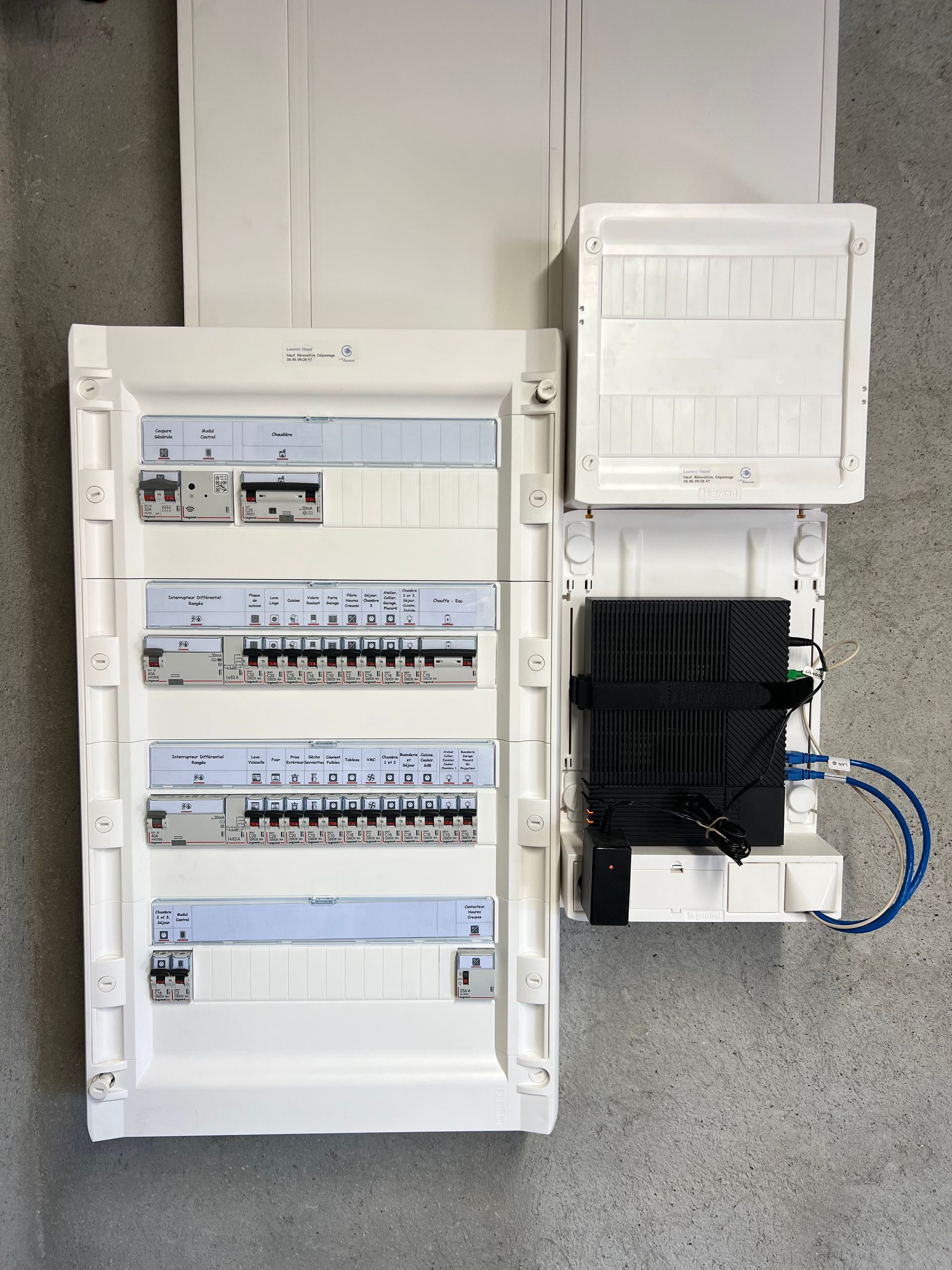 Tableau électrique avec plusieurs disjoncteurs et boîtes de distribution à proximité, sur un mur en béton