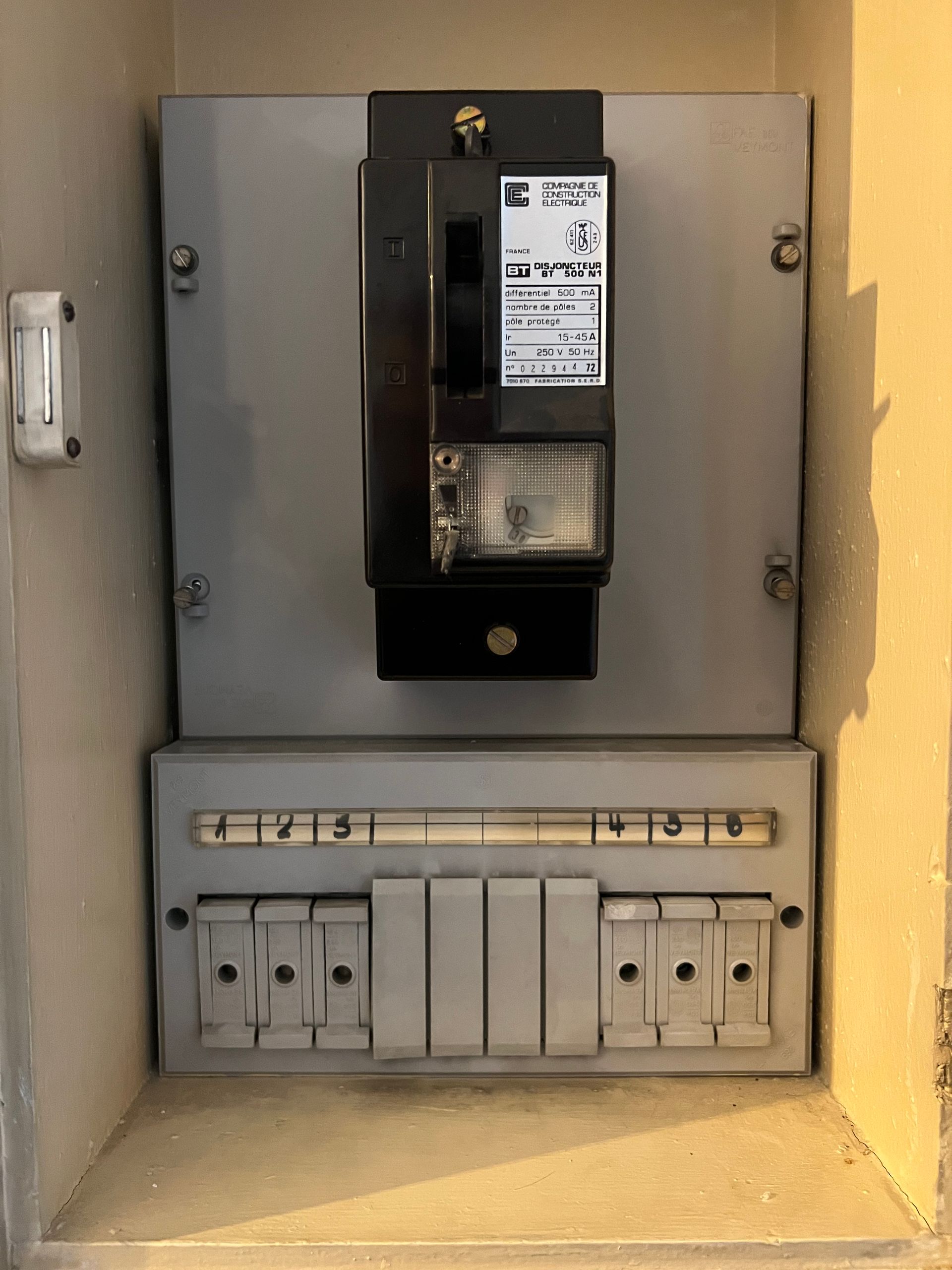 Tableau électrique encastré dans une niche murale, avec le compteur principal au-dessus et les disjoncteurs de plus petits circuits en dessous.