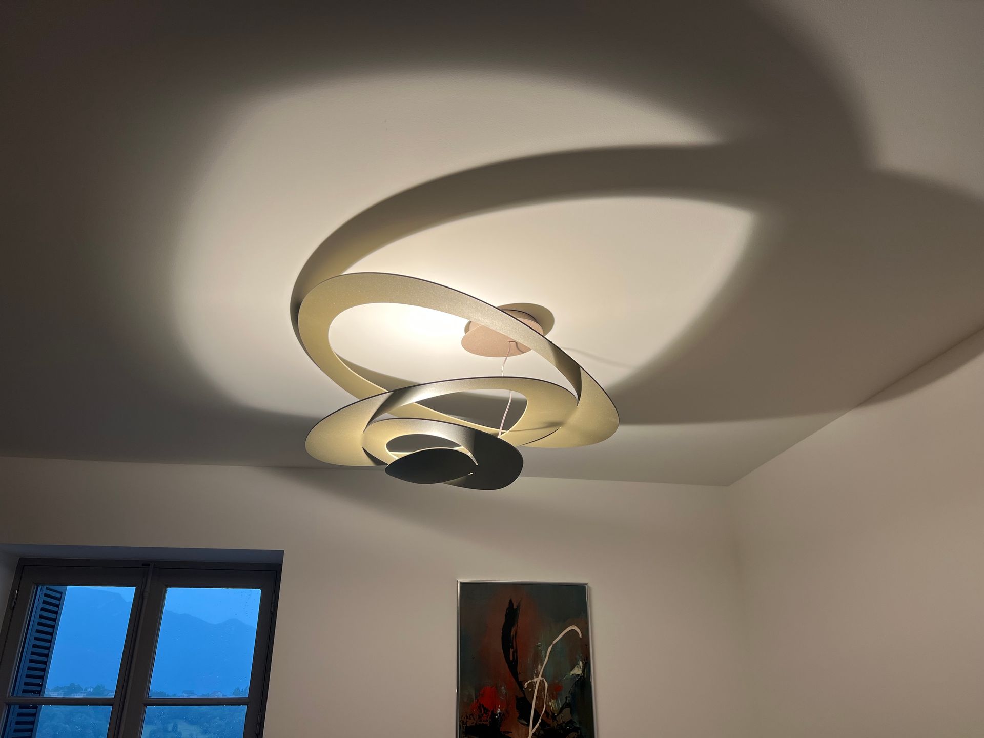 Plafonnier moderne avec anneaux incurvés blancs et noirs projetant des ombres sur un plafond blanc