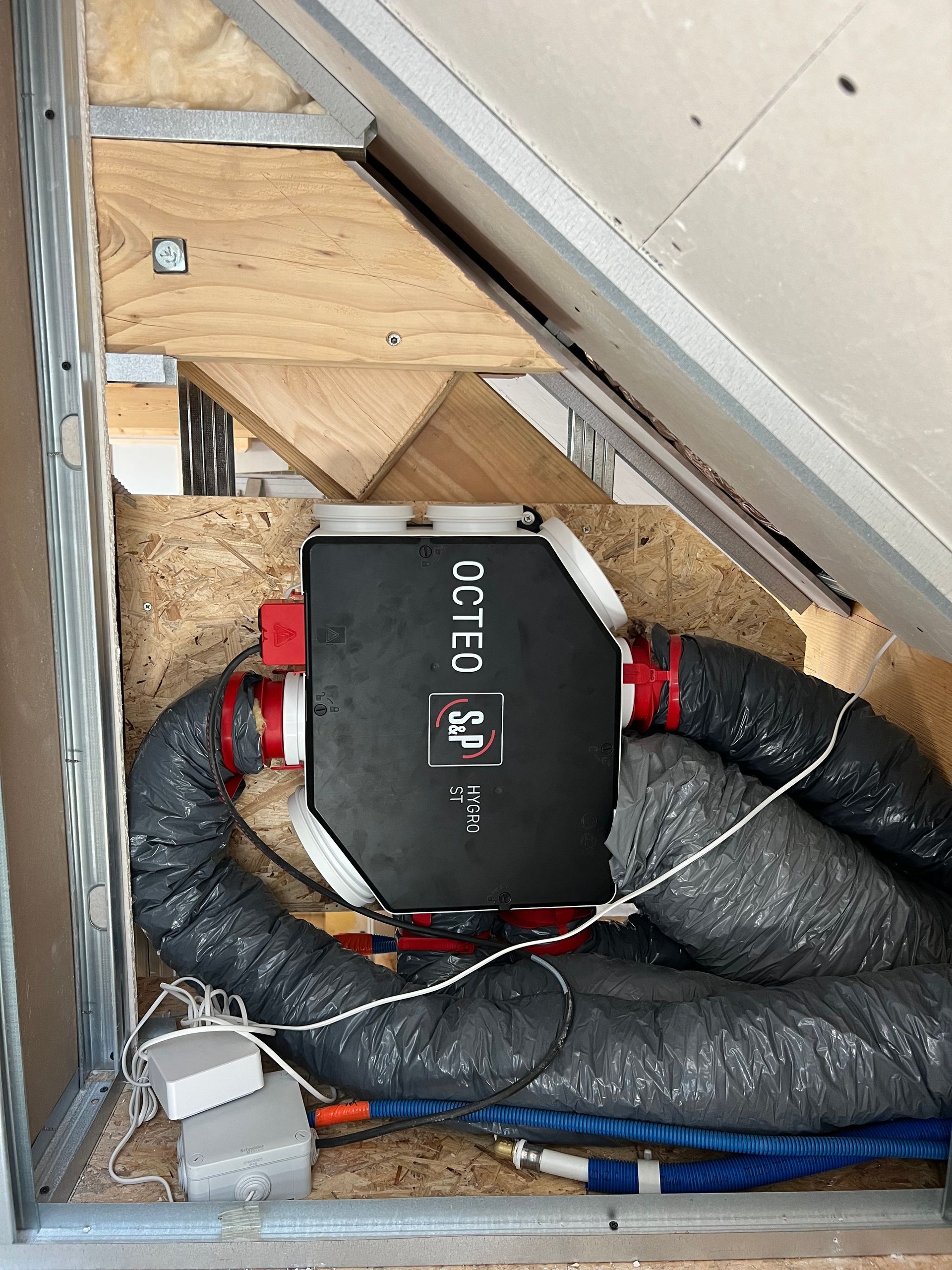 Appareil COTEC noir avec raccords rouges et tuyaux isolés enroulés dans un grenier à ossature bois