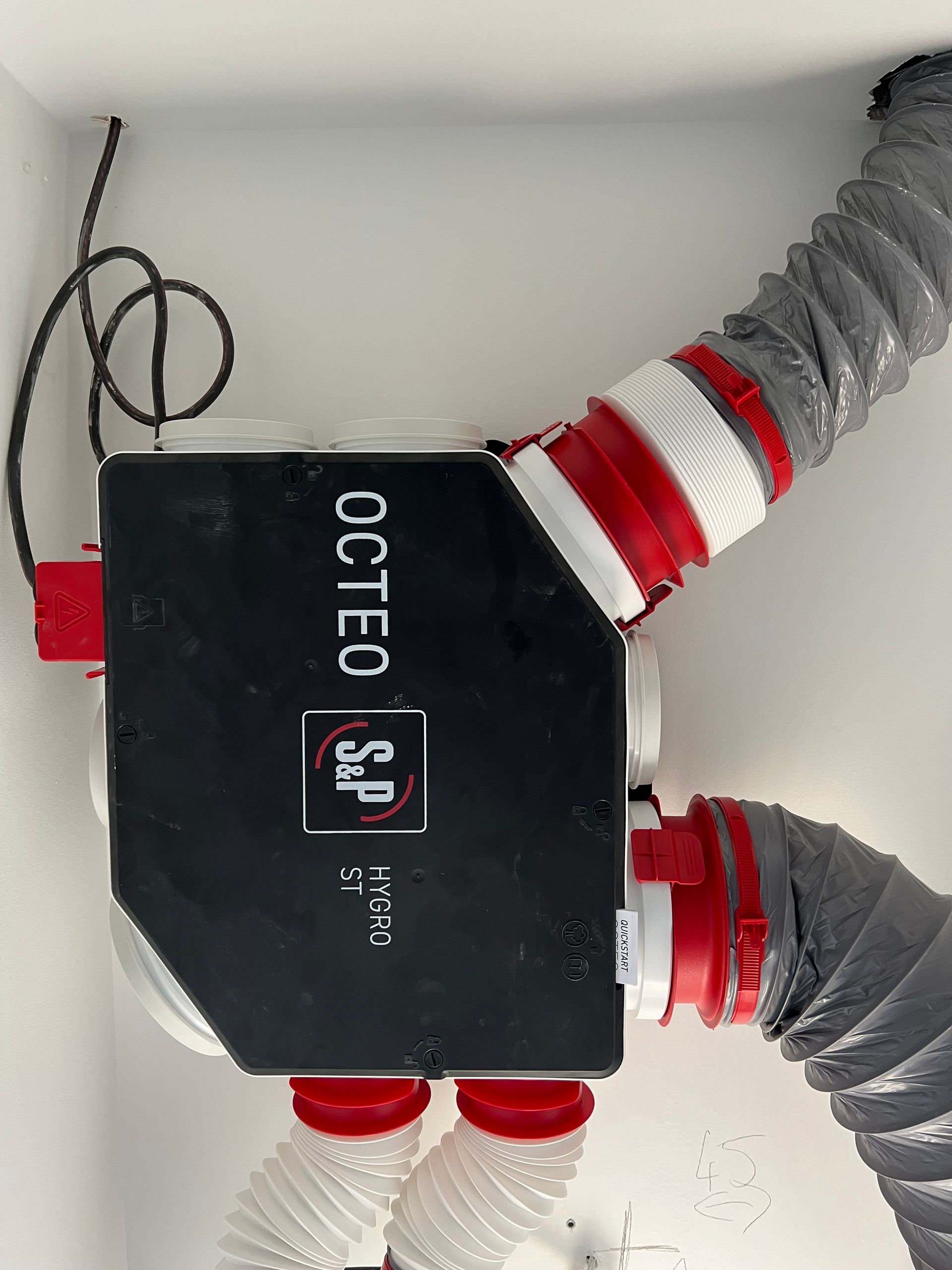Unité de ventilation OCTOPUS noire avec conduits rouges et gris fixés au mur