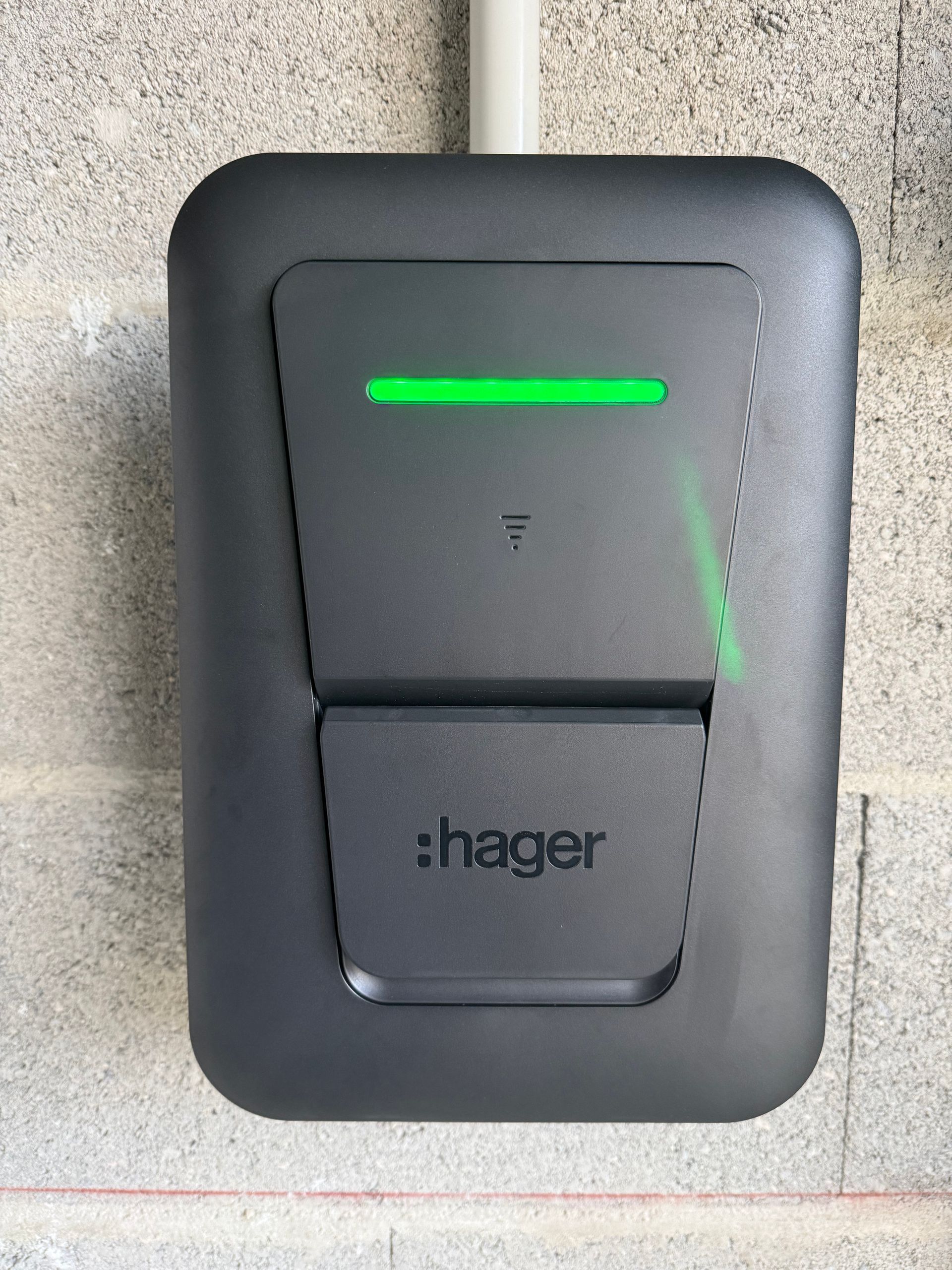 Borne de recharge électrique Black Hager avec voyant vert sur un mur en béton