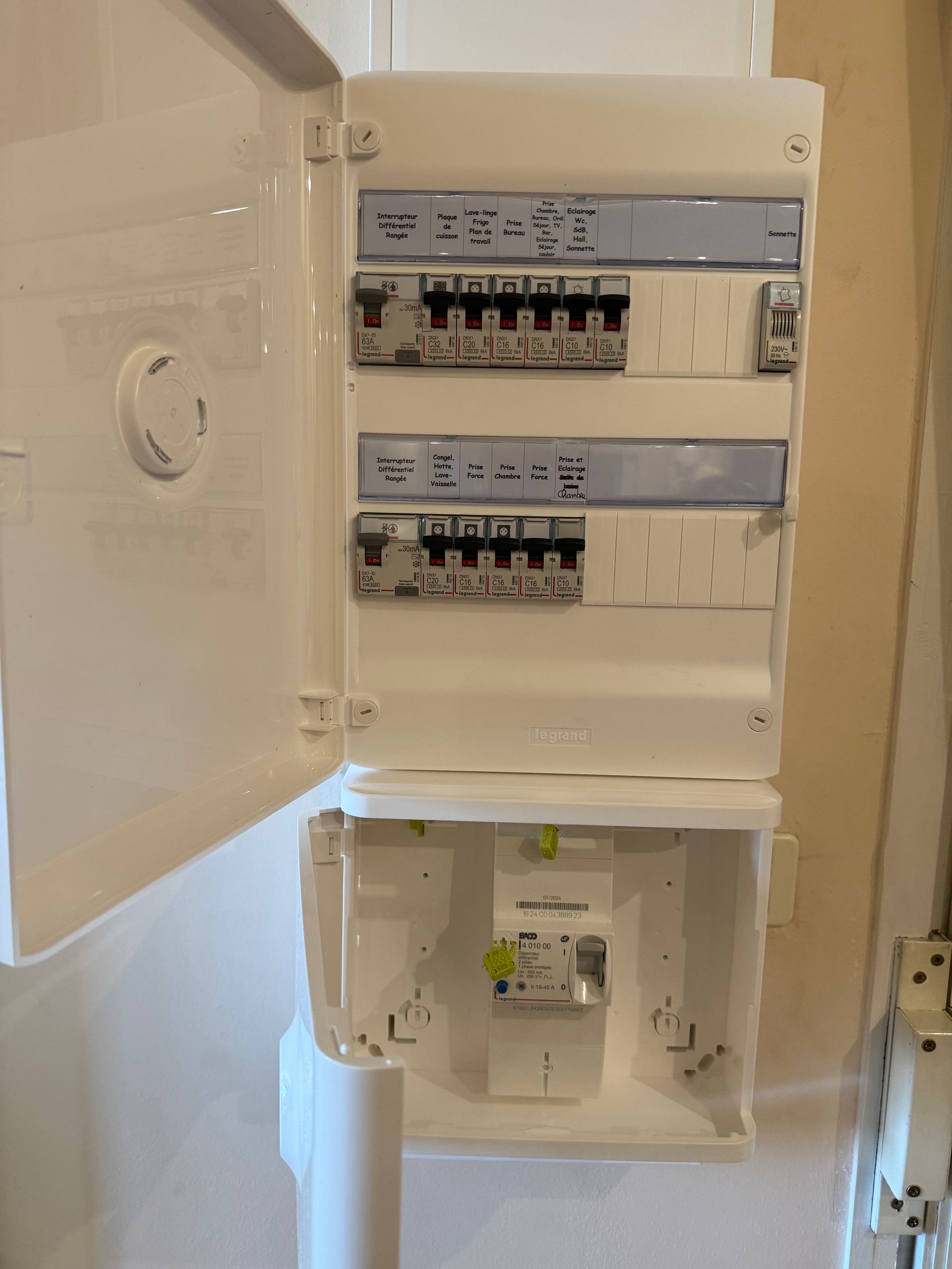 Tableau électrique ouvert avec plusieurs interrupteurs sur un mur, porte entrouverte.