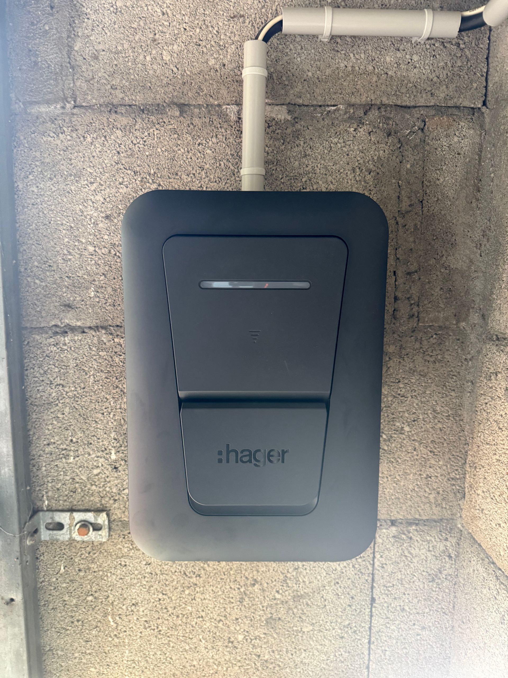 Borne de recharge pour véhicule électrique, installée sous des tuyaux apparents sur un mur en béton.
