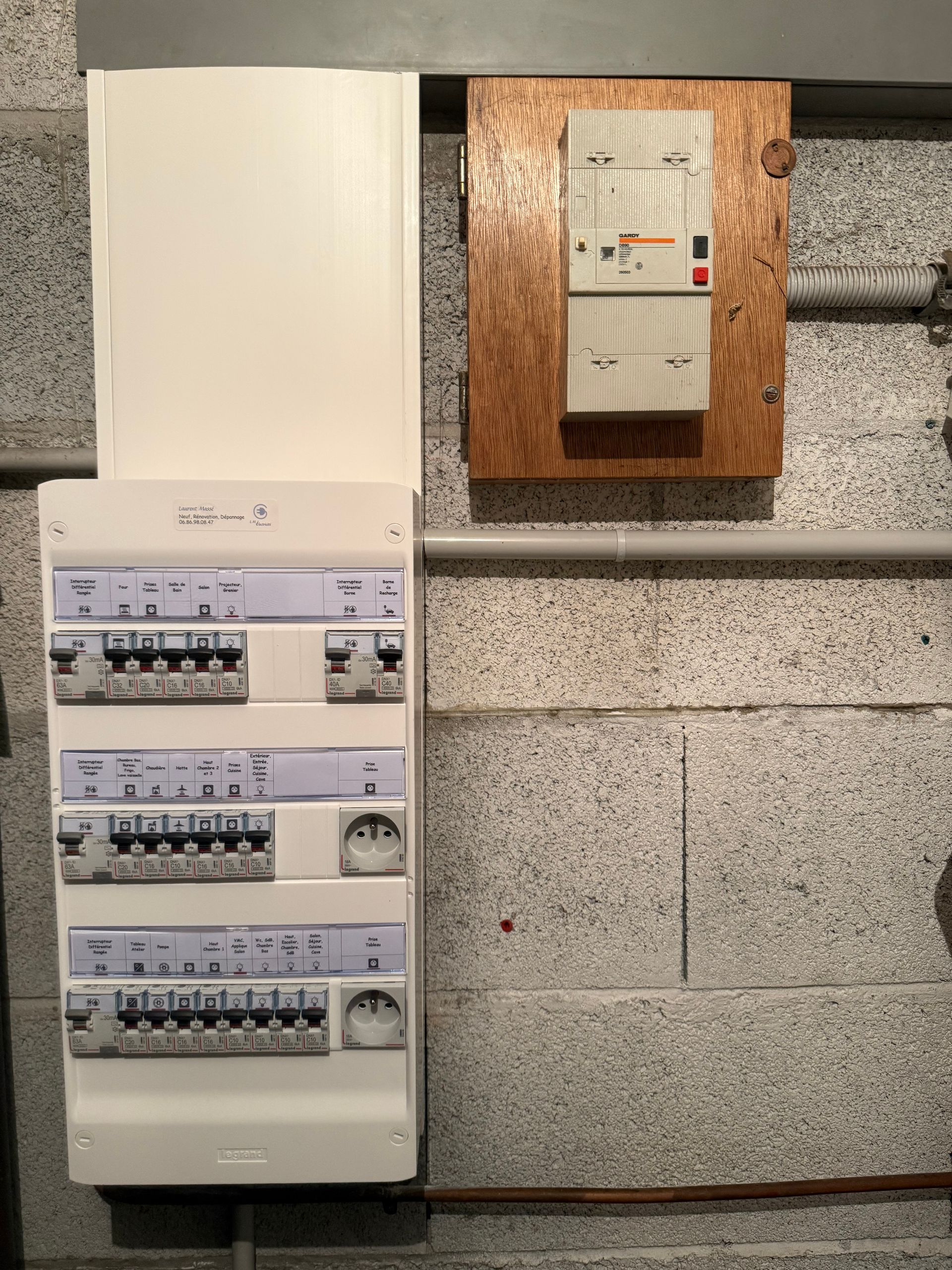 Tableau électrique et boîte de distribution fixés sur un mur en béton dans une buanderie.