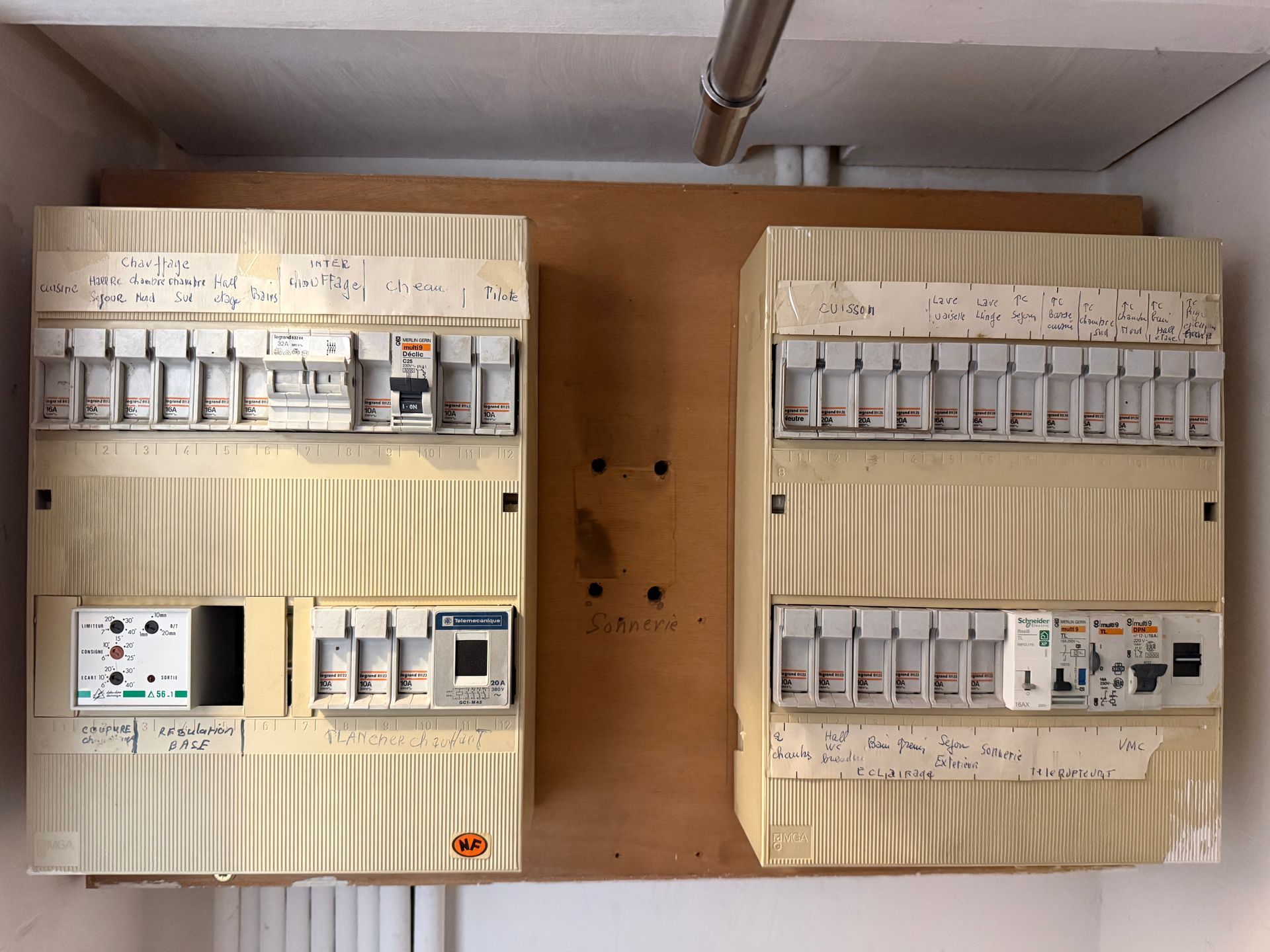 Deux panneaux de disjoncteurs électriques beiges montés sur une planche en bois, avec des rangées d'interrupteurs et de compteurs.