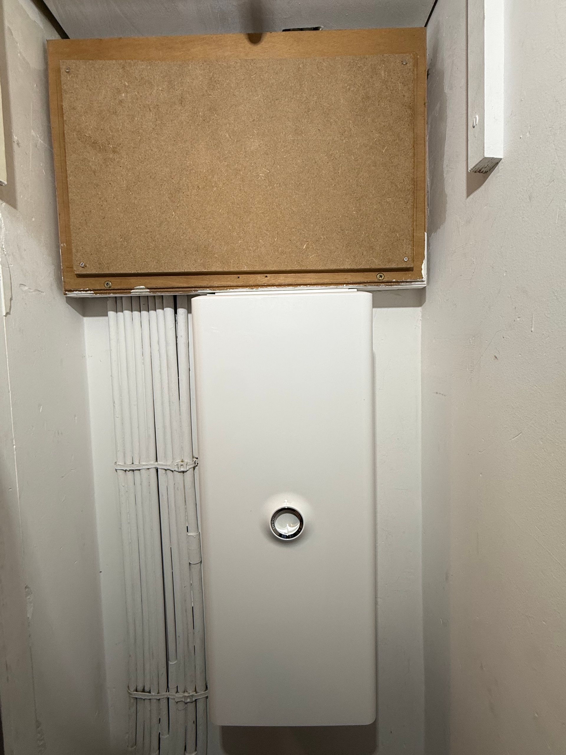 Placard utilitaire étroit avec un tableau électrique blanc et un panneau de liège au-dessus.