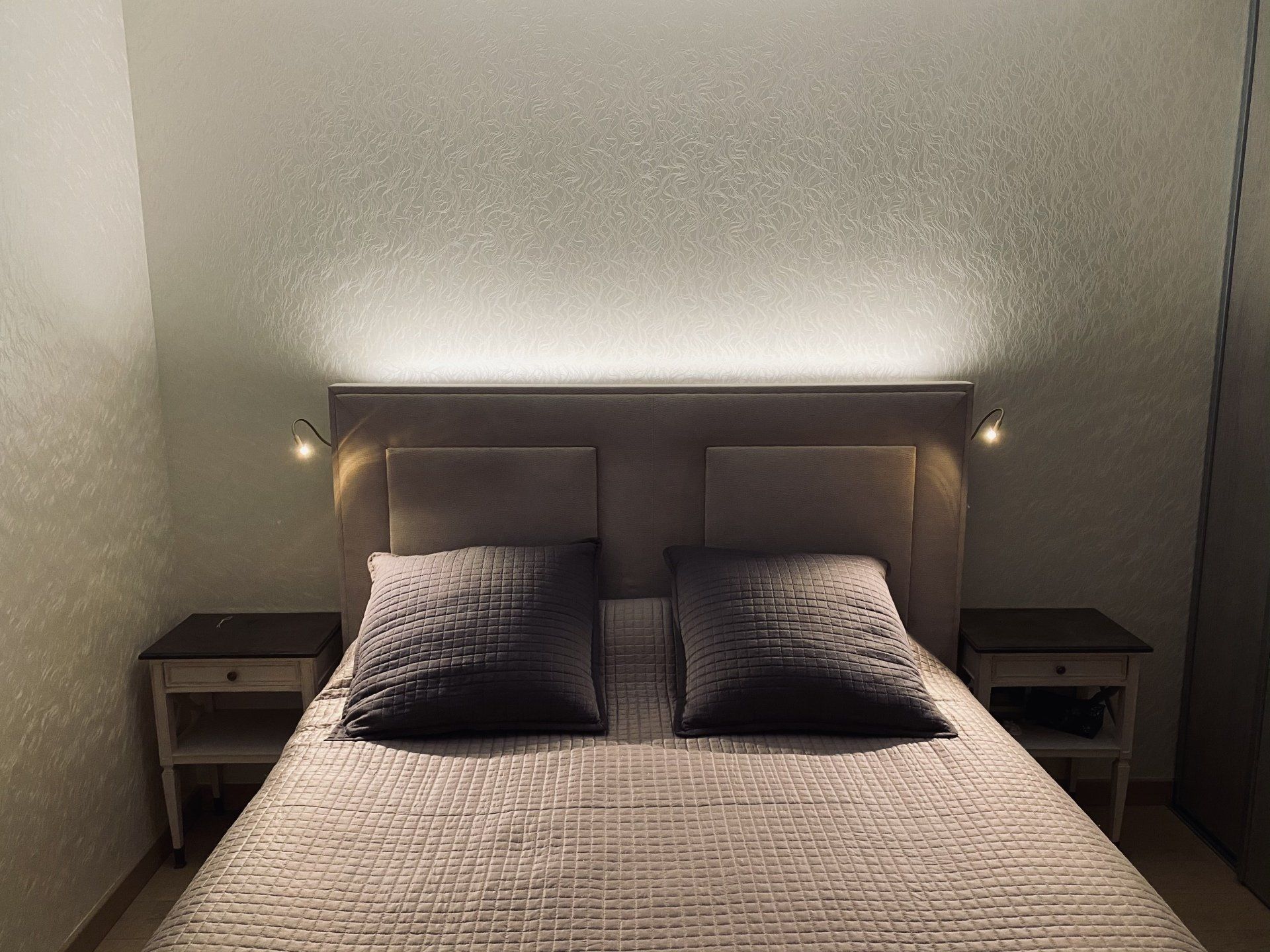 Chambre moderne avec un lit double, deux oreillers, des tables de chevet et des appliques murales à lumière chaude