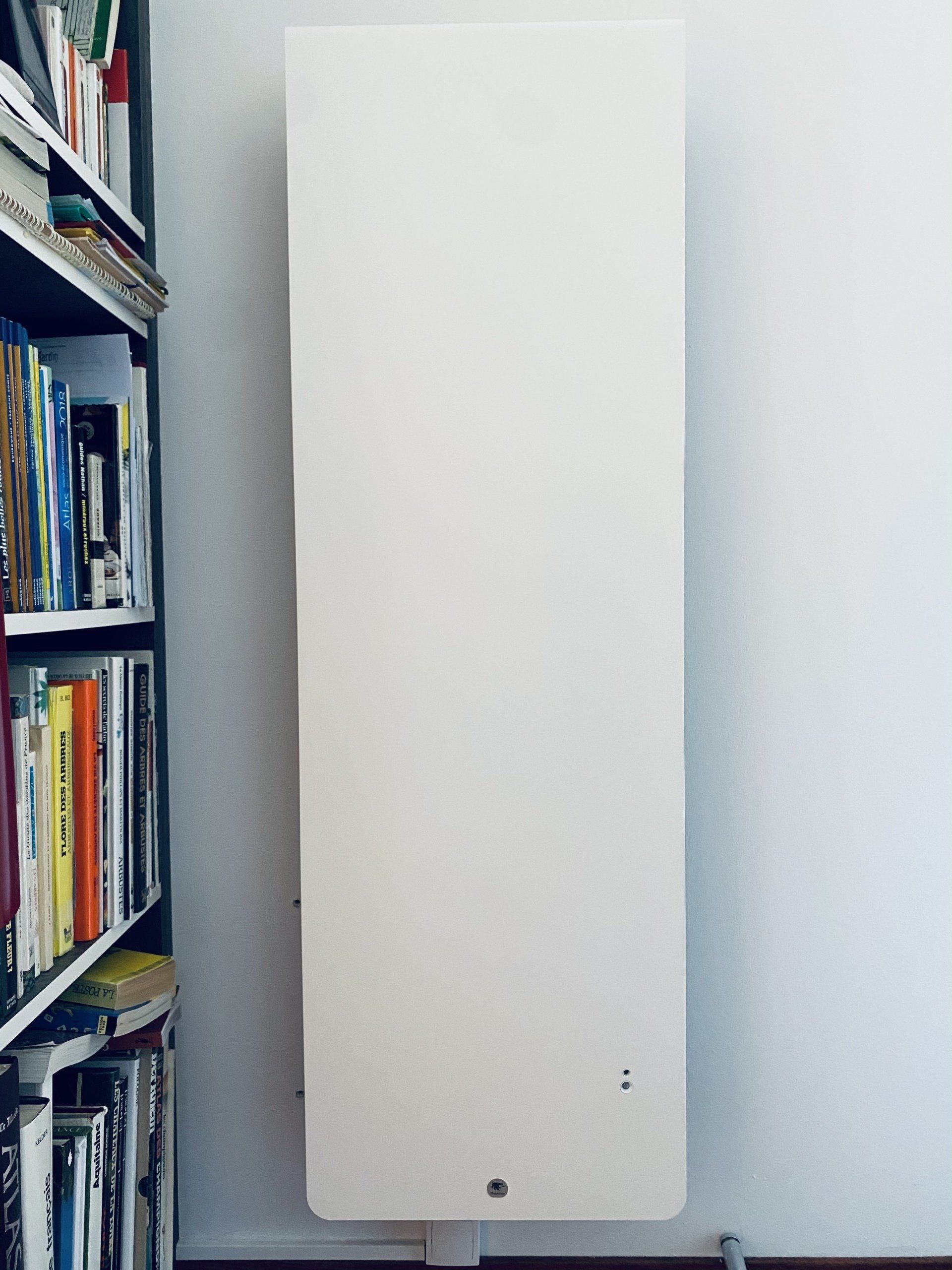 Radiateur blanc fixé au mur à côté d'une bibliothèque dans une pièce