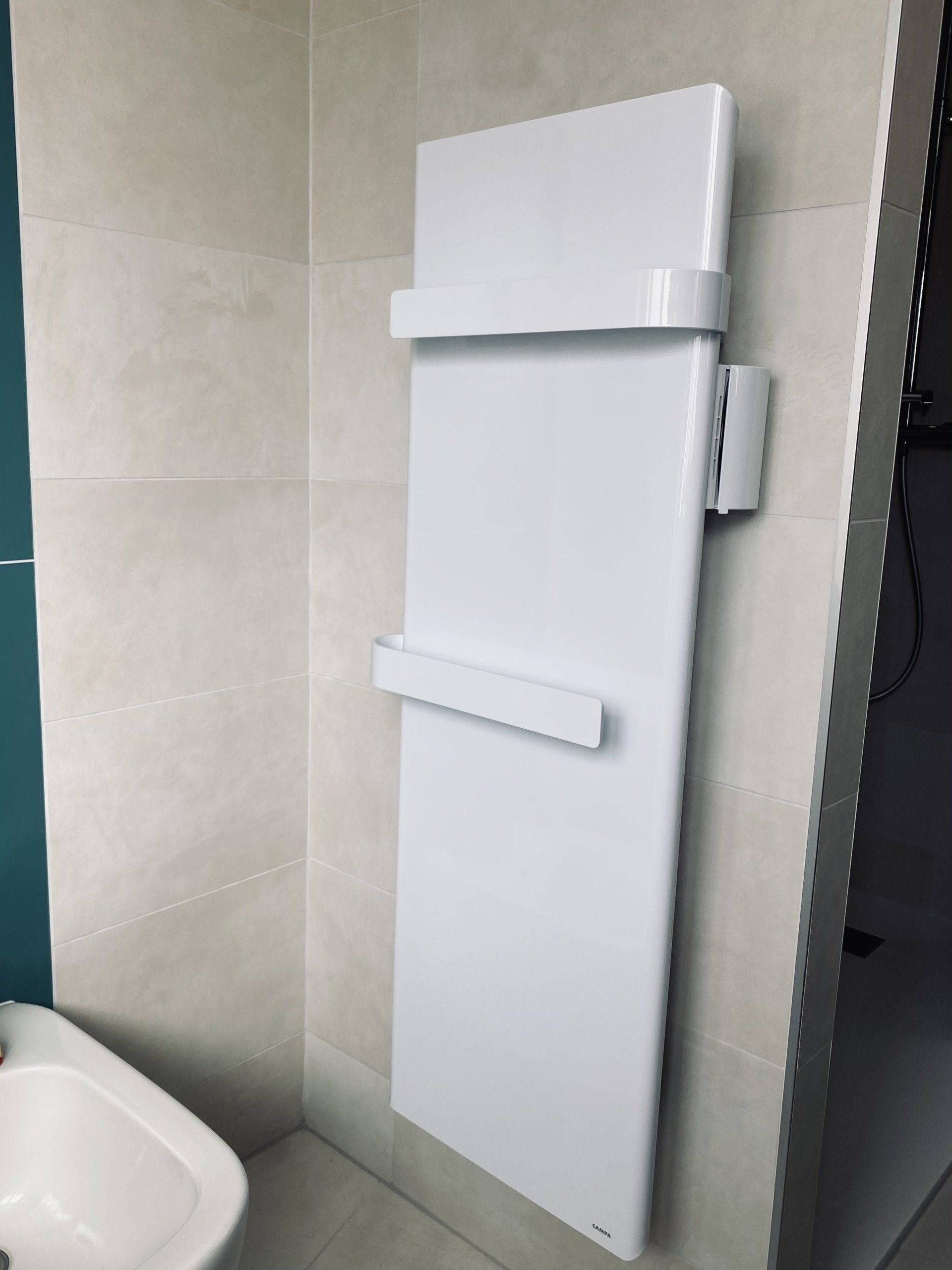 Radiateur/sèche-serviettes mural blanc dans une salle de bain carrelée, à côté d'un lavabo.