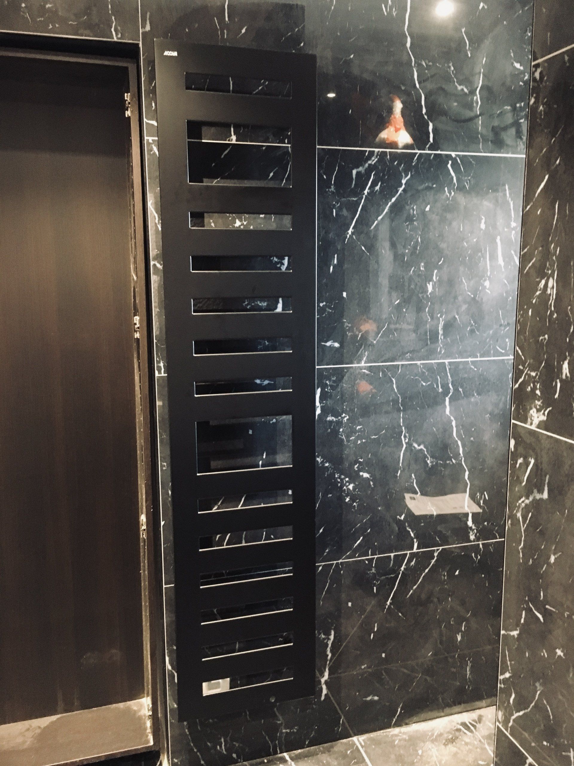 Mur en marbre noir avec un radiateur électrique vertical à côté d'une porte.