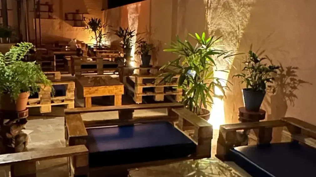 Zona de estar al aire libre con muebles de palets de madera, plantas e iluminación ambiental.