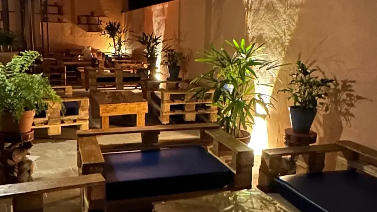 Zona de estar al aire libre con muebles de palets de madera, plantas e iluminación ambiental.